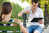 Man using a digital tablet with a woman sitting in front of him, Jardin des Tuileries, Paris, Ile-de-France, France