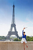 Woman holding a replica of Eiffel Tower sitting on a stone wall with the Eiffel Tower in the background, Paris, Ile-de-France, France