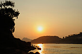 Sonnenuntergang über dem Mekong, Menschen verlassen eine Fähre, Boote am Ufer im Mekong bei Luang Prabang, Laos, Südostasien, Asien