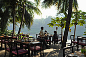 Restaurant terrace under palm trees at Nam Khan river, tributary to Mekong river, Luang Prabang, Laos, Lao Peoples Democratic Republic