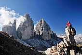 Woman sitting on a rock tower in front of the three peaks, Tre Cime di Lavaredo, Sexten Dolomites, Dolomites, UNESCO World Heritage Site, South Tyrol, Italy