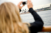 Blond woman photographing Sydney Opera House and harbor, Sydney, Australia