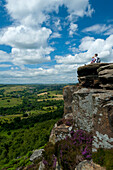 Mother and young girl sitting on rocks admiring view at Froggatt Edge across the Peak District, Froggatt, Derbyshire, England