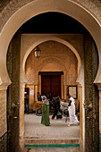 People walking past orange and egg sellers outside entrance to Medersa Bou Inania, Fez, Morocco