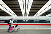 Woman with push chair and young girl walking past train, Munich, Germany