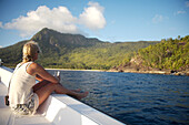 Woman sitting on side of boat heading towards island, Seychelles