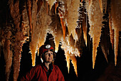 Speleology, caving, caver looking at big orange stalactites