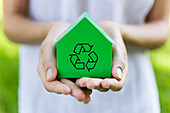 Young woman holding green model house with recycling sign