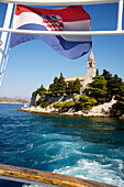 Croatian flag waving in wind with church in distance, Lopud, Elafti Islands, Croatia.