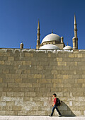 Tourist walking past large wall with Mohammed Ali Mosque behind in Citadel of Cairo, Cairo Egypt