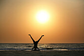Silhouettes of man doing yoga by ocean on the beach at sunset, Arambol, Goa, India