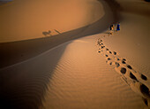 Blue man and camel walking up dune in the desert, Tinfou near Zagora, Morocco