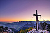 Cross at summit of Soinwand with view to lake Chiemsee, valley of Inn, Chiemgau range and Berchtesgaden range at dawn, view from Wendelstein range, Bavarian alps, Upper Bavaria, Bavaria, Germany, Europe