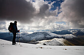 Hiker overlooking snow covered Newlands Valley, Lake District, England