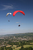 Two people paragliding over Cotswolds escarpment above National Trail, Cheltenham, Gloucestershire, England, UK