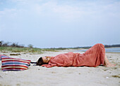 Woman cuddles up in a blanket on the beach in the early evening, Shelter Island, Long Island, New York State, USA