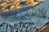 Tussock covered ridge at dawn, partly covered by winter snow, above sea of cloud over Lake Wanaka, Central Otago, Southern Alps, New Zealand