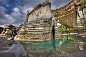 Cliff detail and reflection of algae colours in black sand beach, Tongaporutu, North Taranaki