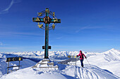 Woman backcountry skiing in front of a cross on the summit of Kleiner Gilfert, Tuxer mountain range, Tyrol, Austria