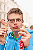 Young man holding two ice-cream cones and pulling a funny face, MR, Leipzig, Sachen, Germany
