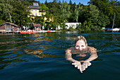 Young woman swimming in lake Starnberg, castle Unterallmannshausen in the background, Bavaria, Germany, Europe