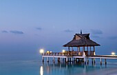 Gazebo and jetty with straw roof at a resort in the Maldives at dusk
