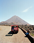 Driver and van with USA flag on the road in front of the volcano Pico de Fogo, 2.829 m high, Cha das Caldeiras, Island of Fogo, Ilhas do Sotavento, Republic of Cape Verde, Africa