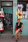 Eine Frau sitzt vor einem Geschäft mit Che Guevara Souvenirs, Havanna, Havana, Kuba, Karibik