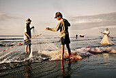 Fishermen folding their nets on the beach after work, Mui Ne fishing village, Vietnam, South China Sea