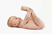 BABY, BOY PLAYING WITH HIS FEET AGAINST WHITE BACKGROUND