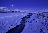 Moonlight reflects against the snow on Borgarfjordur fjord, on the west end of Iceland