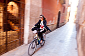 Young woman on her bike in an alley, Street scene in Palma, view into the Palau Palma de Mallorca, Mallorca, Spanien