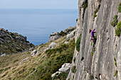Junge Frau klettert in steiler Wand, Wandern und Klettern auf Mallorca, Klettergebiet am Cap de Formentor, Blick auf das Mittelmeer, La Creveta, Cap de Formentor, Serra de Tramuntana, Unesco World Cultural Heritage, Mallorca, Spanien