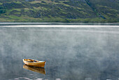 A single wooden rowing boat moored, anchored, floating on the still waters of  Loch Maree. A freshwater loch. Mist rising., Loch Maree, Wester Ross Scotland