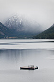 A fishing boat on the flat calm waters of Wallowa Lake in Northeast Oregon. Mountains rising steeply from the water. Low cloud. Spring., Wallowa Lake in Northeast Oregon