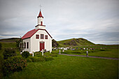 A traditional church with a spire and a red roof. A graveyard or cemetery., Icelandic church in a remote setting