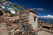 View of Lake Manasarovar from Chiu Monastery. A small Buddhist temple and monastery building on the hillside. Flat calm waters of the lake. Prayer flags., Lake Manasarovar, Tibet Autonomous Region
