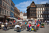 Menschen sitzen draußen vor einem Café und genießen einen sonnigen Sonntag vormittag am Domplatz, mit dem legendären Restaurant Maison Kammerzell im Hintergrund, Straßburg, Elsass, Frankreich, Europa