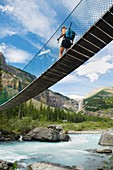 Hiker crossing suspension bridge on the Berg Lake Trail, Mount Robson Provincial Park British Columbia Canada