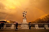 tourists with umbrellas and a rainbow over an angel the Bridge of Angels, Rome, Italy, Europe