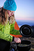 Young woman cooking noodles beside a tent, Risserkogel, Bavarian Prealps, Mangfall Mountains, Bavaria, Germany