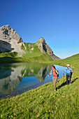 Two hikers walking in front of lake Rappensee with Hochrappenkopf and Kleiner Rappenkopf, Allgaeu range, Upper Allgaeu, Allgaeu, Swabia, Bavaria, Germany