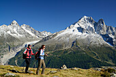 Woman and man hiking with view to Aiguille du Chardonnet, Aiguille d' Argentiere, Aiguille Verte and Grand Dru, Mont Blanc range, Chamonix, Savoy, France