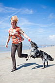 Frau spielt mit einem Hund am Strand, Zandvoort, Nordholland, Niederlande