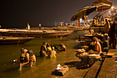 Menschen waschen sich während ein Heiliger Mann betet, am Dasaswamedh Ghat am Ufer des Fluss Ganges, Varanasi, Uttar Pradesh, Indien