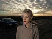 Businesswoman walking in parking lot. Sunrise in car park with car in back ground and girl in coat in foreground