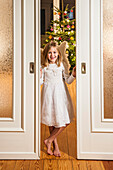 Girl wearing an angel costume looking through a sliding door, christmas tree in background, Hamburg, Germany