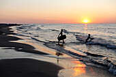 Two children running into the sea, wakeboard, sunset, waves, Baltic Sea, beach near Bakenberg, Wittow Peninsula, Island of Ruegen, Mecklenburg West-Pomerania, Germany