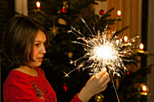 Girl holding a sparkler, christmas tree in background