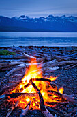 Campfire at dusk on a remote coastal beach in Goose Cove with Fairweather Range in the background, Muir Inlet, Glacier Bay National Park & Preserve, Southeast Alaska, Summer